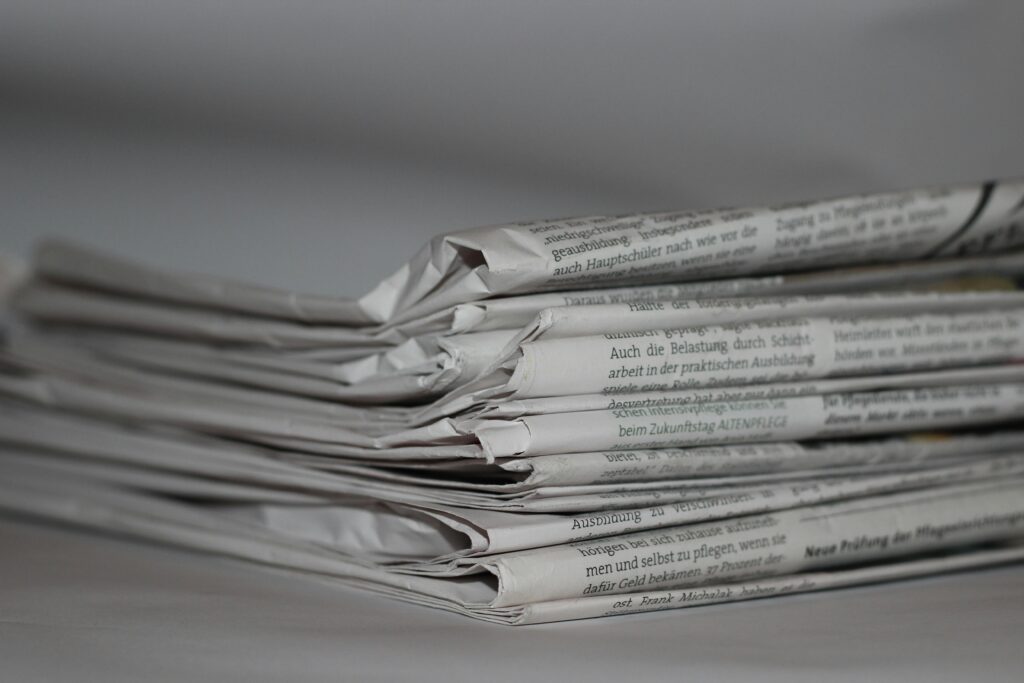 News – czym jest i jak wpływa na nasze postrzeganie świata? Stos gazet na biurku – co to jest news, aktualności i informacje w mediach tradycyjnych oraz online