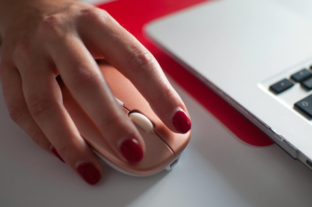 Clickbait – co to jest, przykłady i wpływ na SEO Dłoń klikająca myszkę komputerową przy laptopie – ilustracja clickbaitowych nagłówków zachęcających do kliknięcia w internecie