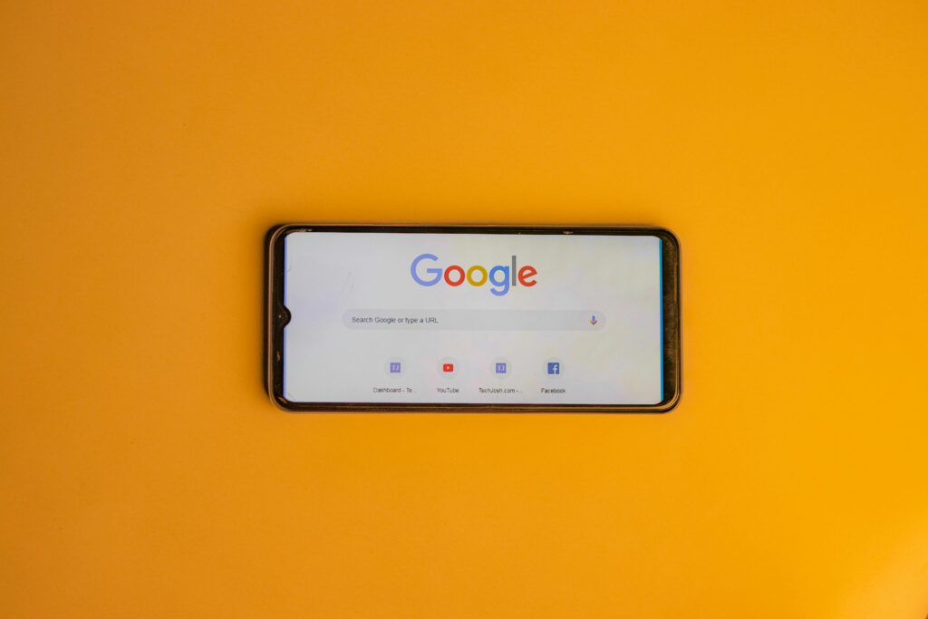 Smartfon z wyszukiwarką Google na żółtym tle symbolizujący Google Ads Google i kampanie reklamowe w wynikach wyszukiwania.