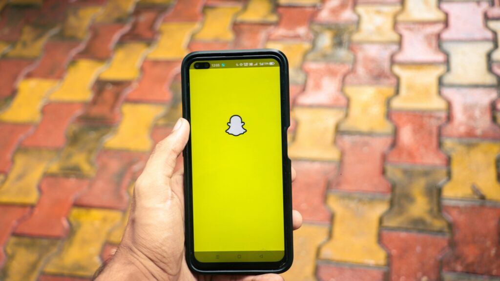 Smartfon z otwartą aplikacją Snapchat na żółtym ekranie – co to promo na Snapie, czyli płatna promocja treści zwiększająca zasięg, wyświetlenia i rozpoznawalność marki wśród użytkowników.