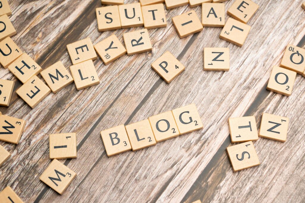 Drewniane klocki z napisem „BLOG” na tle rozsypanych liter – jakie są zalety pisania i prowadzenia bloga w kontekście budowania marki, zwiększania widoczności SEO i pozyskiwania klientów online.