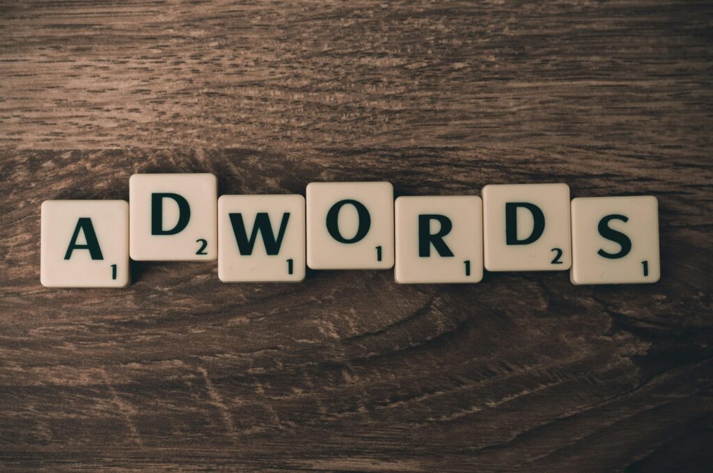 Marketing a reklama – czym się różnią i jak wspólnie budują silną markę? Co to reklama – napis „Adwords” ułożony z liter na drewnianym tle jako symbol marketingu internetowego i promocji.