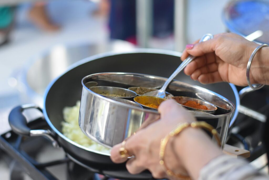 Marketing restauracji – jak skutecznie przyciągnąć więcej gości? Marketing gastronomii – dodawanie przypraw do potrawy na patelni jako symbol strategii promocji restauracji i budowania atrakcyjnej oferty kulinarnej