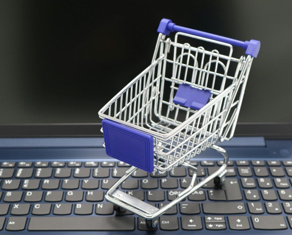 Reklama produktowa w Google – jak zwiększyć sprzedaż w e-commerce? Reklama produktowa Google – miniaturowy wózek zakupowy na klawiaturze laptopa jako symbol kampanii Google Shopping i promocji produktów w wyszukiwarce internetowej