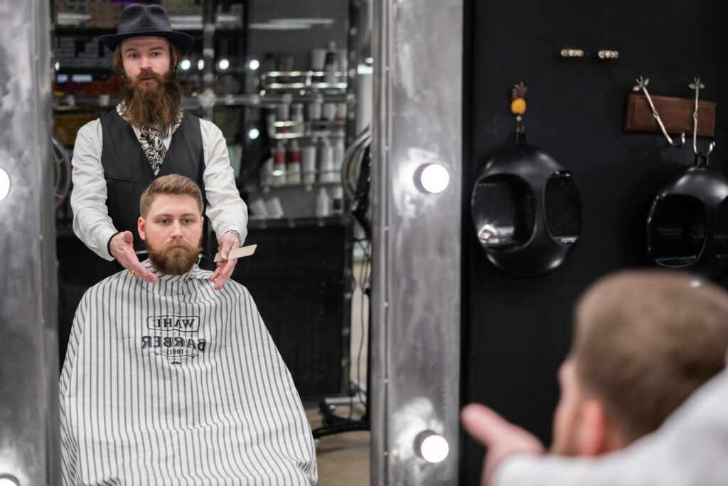 Reklama salonu fryzjerskiego – jak skutecznie przyciągać klientów online? Reklama fryzjerska przedstawiająca profesjonalnego barbera podczas stylizacji brody klienta w nowoczesnym salonie barberskim.