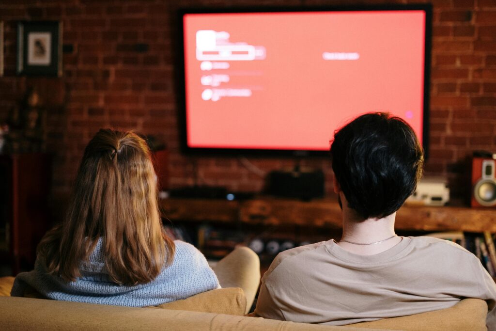 Reklama telewizyjna – przykłady kampanii, które odniosły sukces Reklama przykłady – para oglądająca telewizję z wyświetloną kampanią reklamową jako przykład reklamy w mediach