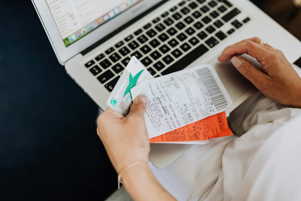Osoba dokonująca zakupu online – płatność kartą przy laptopie, trzymająca paragon i bilet potwierdzający transakcję w e-commerce.