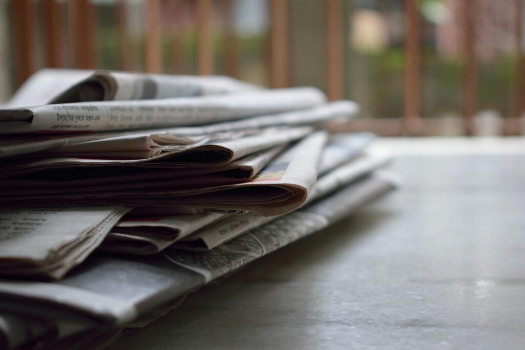 Skuteczne newslettery – przykłady i inspiracje do kampanii e-mail marketingowych Newsletter przykłady – stos gazet i prasy na stole symbolizujący aktualności i komunikację marketingową