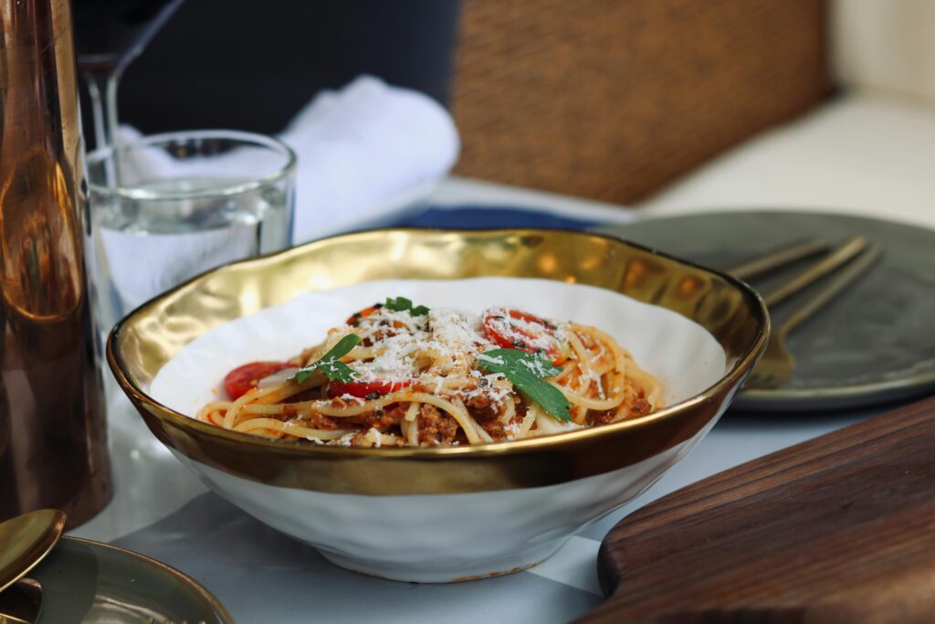 Apetyczny makaron spaghetti z sosem pomidorowym, świeżą bazylią i startym serem w eleganckiej misce – reklama sklepu spożywczego promująca świeże produkty i składniki do domowych dań.