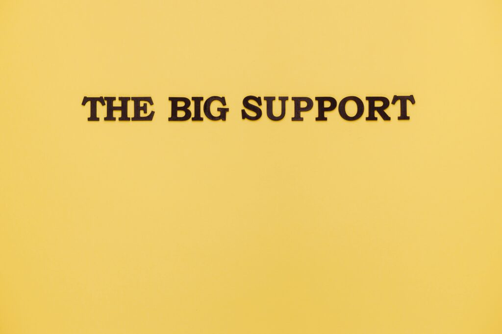 Slogan reklamowy – jak stworzyć hasło, które zapada w pamięć? Slogan reklamowy – napis „The Big Support” na żółtym tle, przykład hasła marketingowego budującego wizerunek marki i przekaz reklamowy.