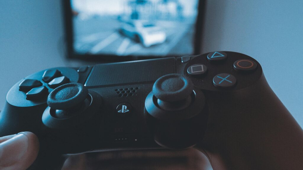 Advergaming – jak gry wideo zwiększają zaangażowanie i rozpoznawalność marki? Advergaming – kontroler do gier przed ekranem symbolizujący wykorzystanie gier wideo w działaniach marketingowych i promocji marki