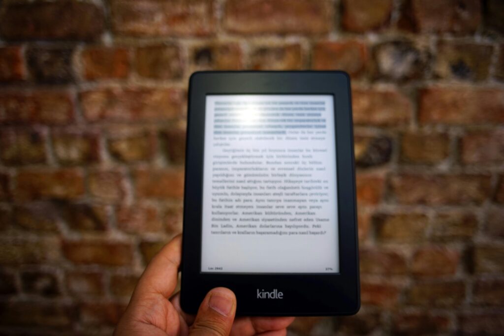 LinkedIn ebook – jak skutecznie rozwijać marketing i sprzedaż na LinkedIn? LinkedIn ebook – czytnik Kindle z otwartym ebookiem na tle ceglanej ściany jako symbol publikacji eksperckiej i marketingu treści na LinkedIn