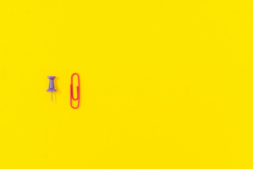 Minimalistyczne elementy biurowe na żółtym tle symbolizujące kampania AdWords i skuteczne przyciąganie uwagi w reklamie Google Ads.